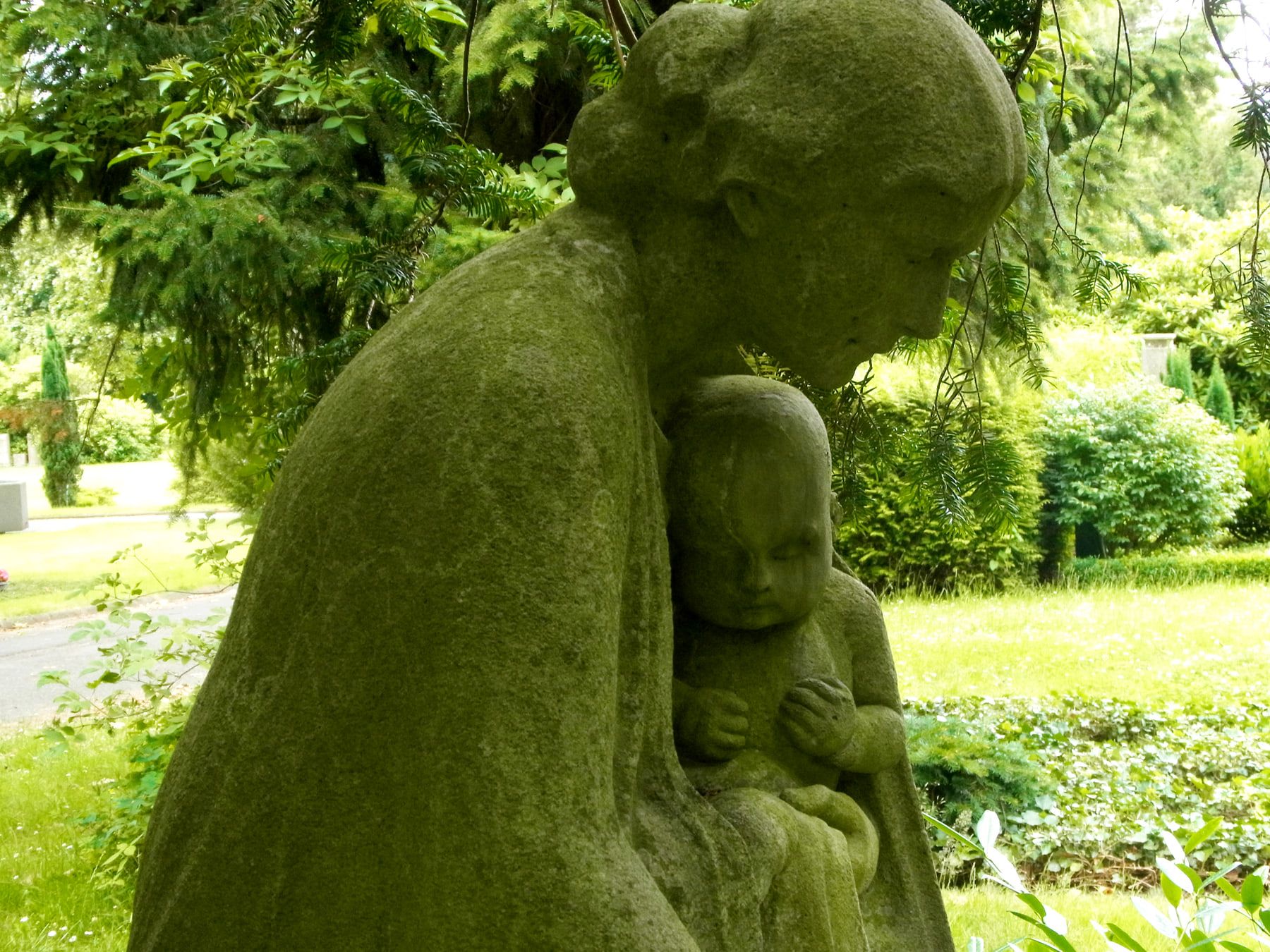 Steinskulptur einer sitzenden Gestalt mit Kind zwischen Grabstätten auf Hauptfriedhof Braunschweig